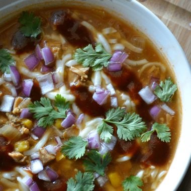 slow cooker barbecue chicken pizza soup in a white bowl on top of a wooden cutting board