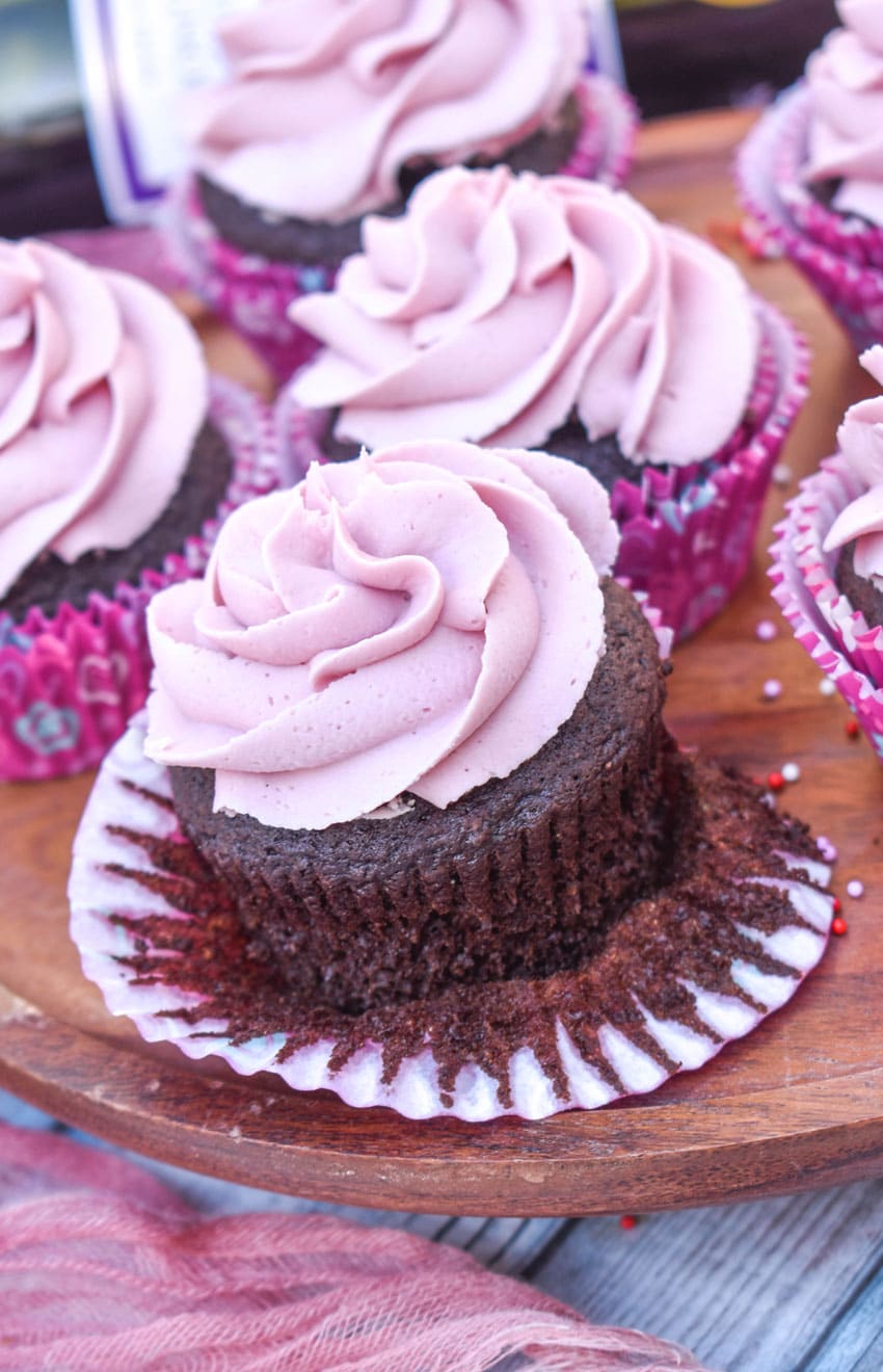 an unwrapped dark chocolate cupcakes with red wine buttercream frosting on a wooden cake stand