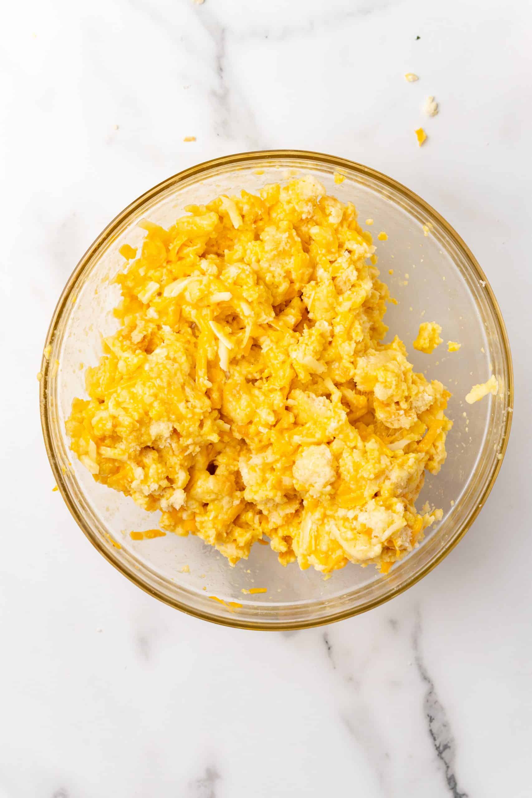 breakfast mac and cheese biscuit topping mixing together in a glass mixing bowl