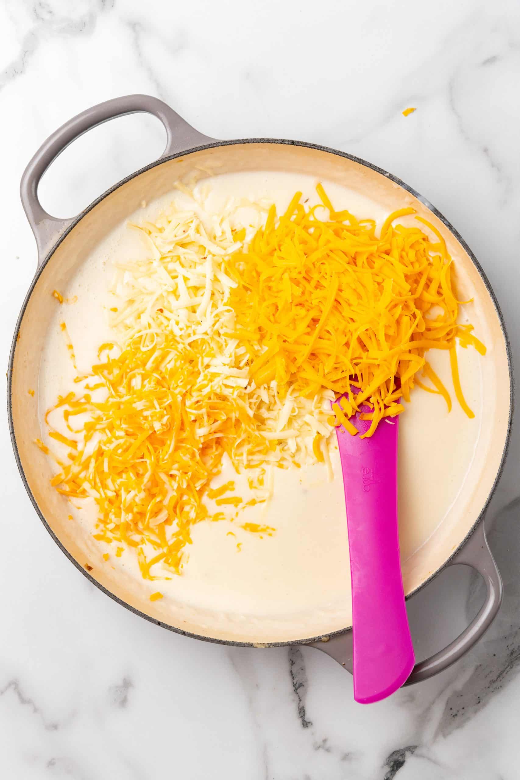 shredded cheese added to a roux in a large gray skillet