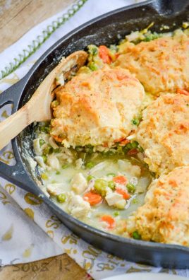 a wooden spoon stuck in a skillet of cheddar bay biscuit topped chicken and vegetable cobbler