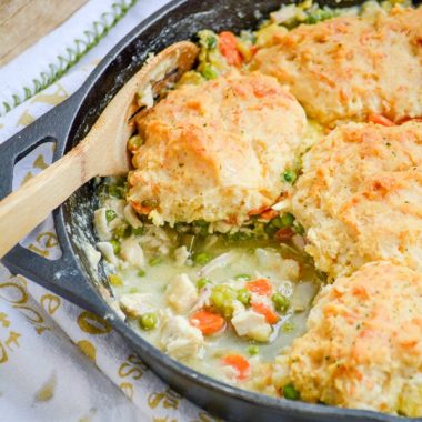 a wooden spoon stuck in a skillet of cheddar bay biscuit topped chicken and vegetable cobbler