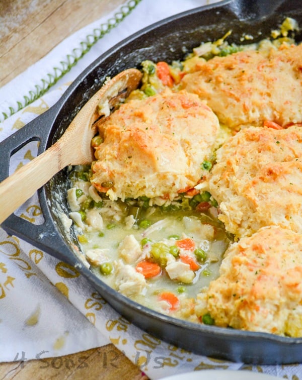 a wooden spoon stuck in a skillet of cheddar bay biscuit topped chicken and vegetable cobbler