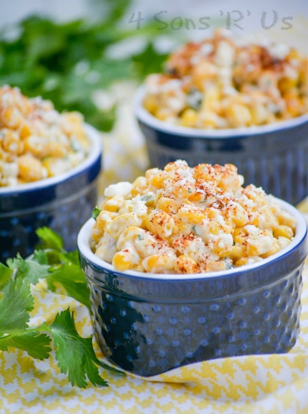 Mexican Street Corn Salad in three blue ramekins on a yellow and white cloth napkin with fresh cilantro in the background