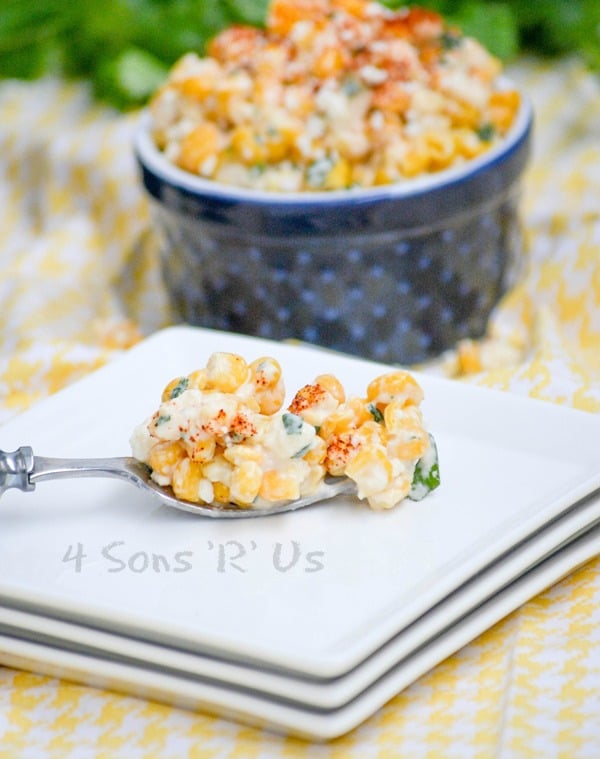 a forkful of Mexican Street Corn Salad shown a top a stack of square white appetizer plates