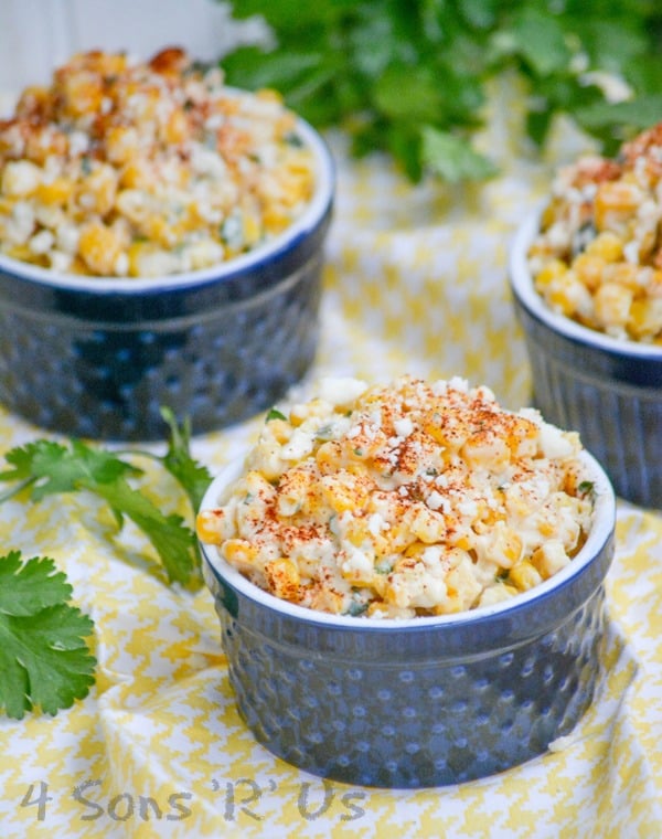 Mexican Street Corn Salad in three blue ramekins on a yellow and white cloth napkin with fresh cilantro in the background