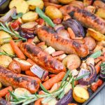 sausage, apple, and herb sheet pan supper shown on a dark sheet pan on a gray background