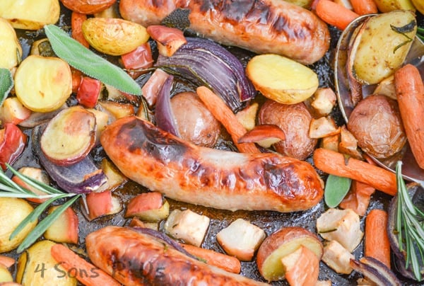 Sausage, Apple, And Herb Sheet Pan Supper shown in a close up focusing on a single charred sausage surrounded by roasted vegetables