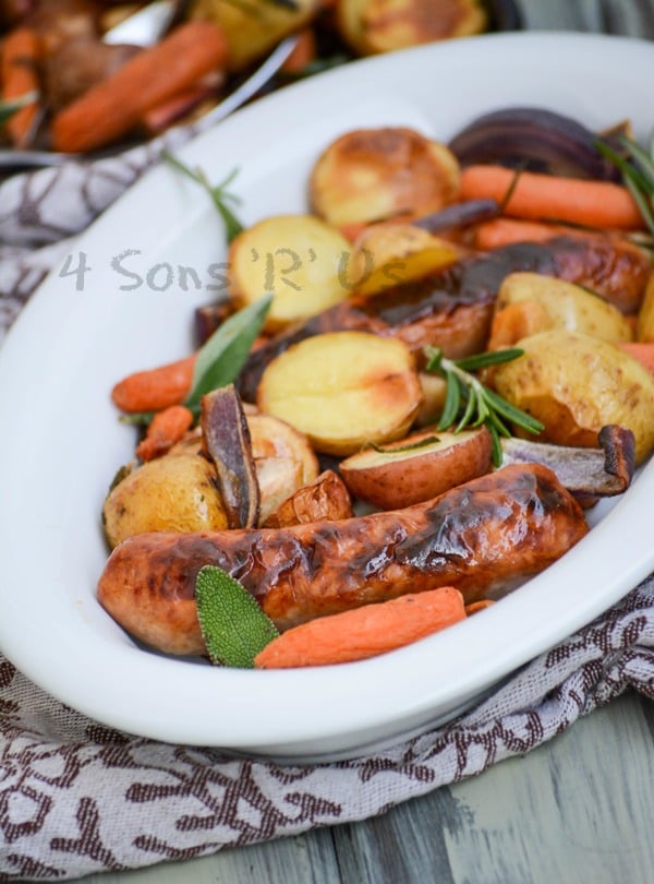 Sausage, Apple, And Herb Sheet Pan Supper shown in a white oval serving dish on a cloth napkin with fresh herbs
