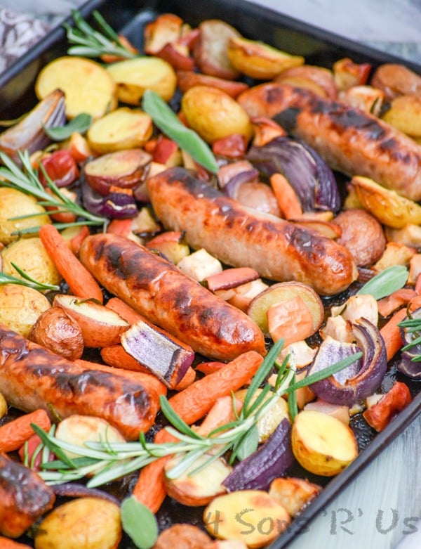 Sausage, Apple, And Herb Sheet Pan Supper shown on a dark sheet pan on a green background