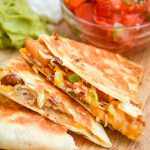 A STACK OF THREE SLICES OF SHRIMP AND BACON QUESADILLAS ON A WOODEN CUTTING BOARD