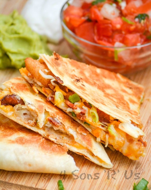 A STACK OF THREE SLICES OF SHRIMP AND BACON QUESADILLAS ON A WOODEN CUTTING BOARD