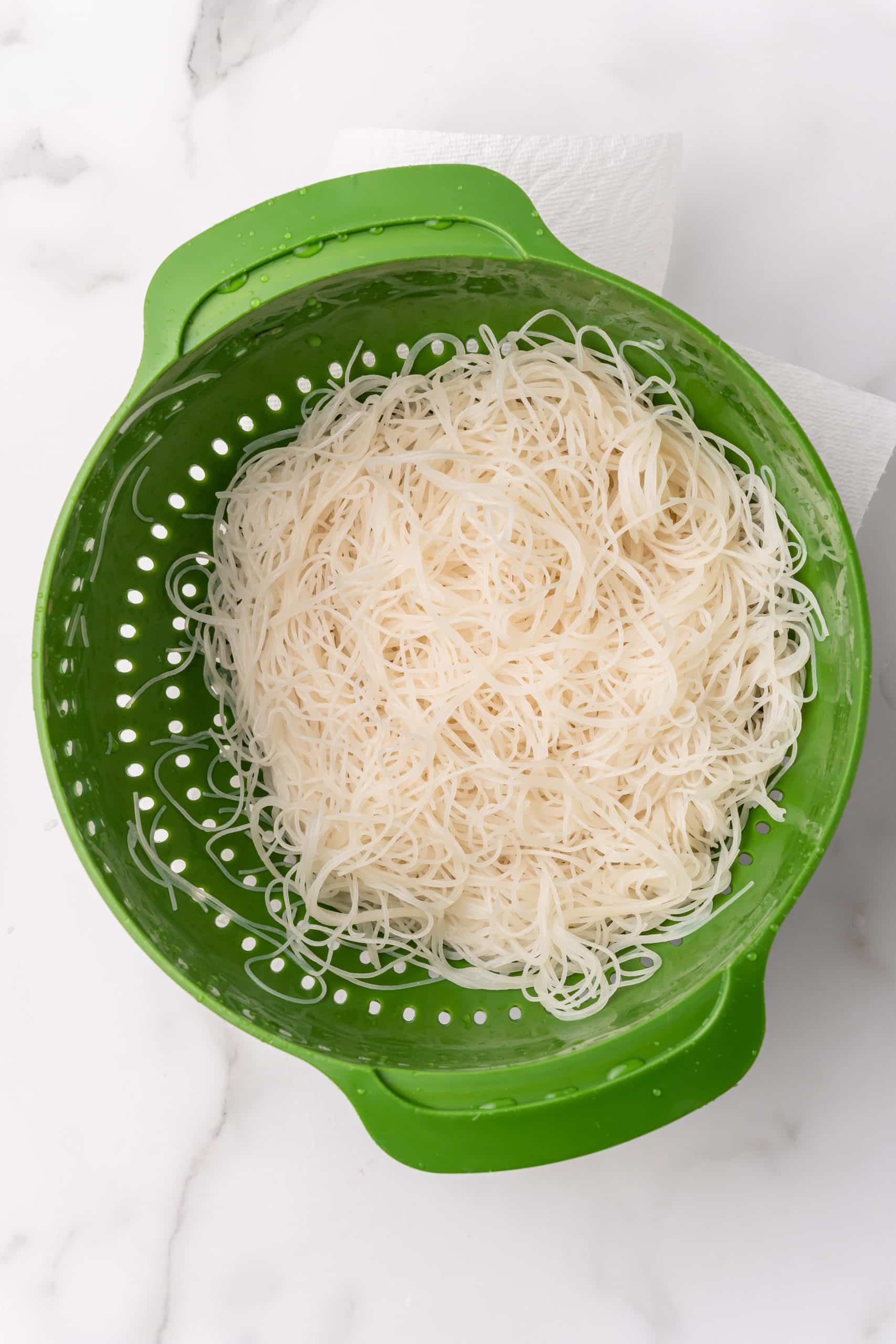 cooked rice noodles in a green strainer