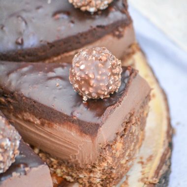 a sliced ferrerro rocher nutella cheesecake on a wooden cutting board