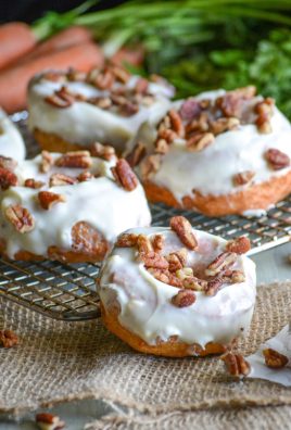 carrot cake donuts with cream cheese glaze topped with chopped nuts and arranged on a wire cooling rack