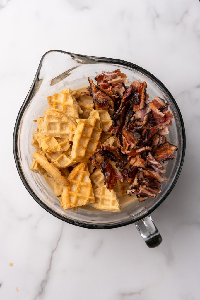 chopped waffles and crispy pieces of bacon in a glass mixing bowl