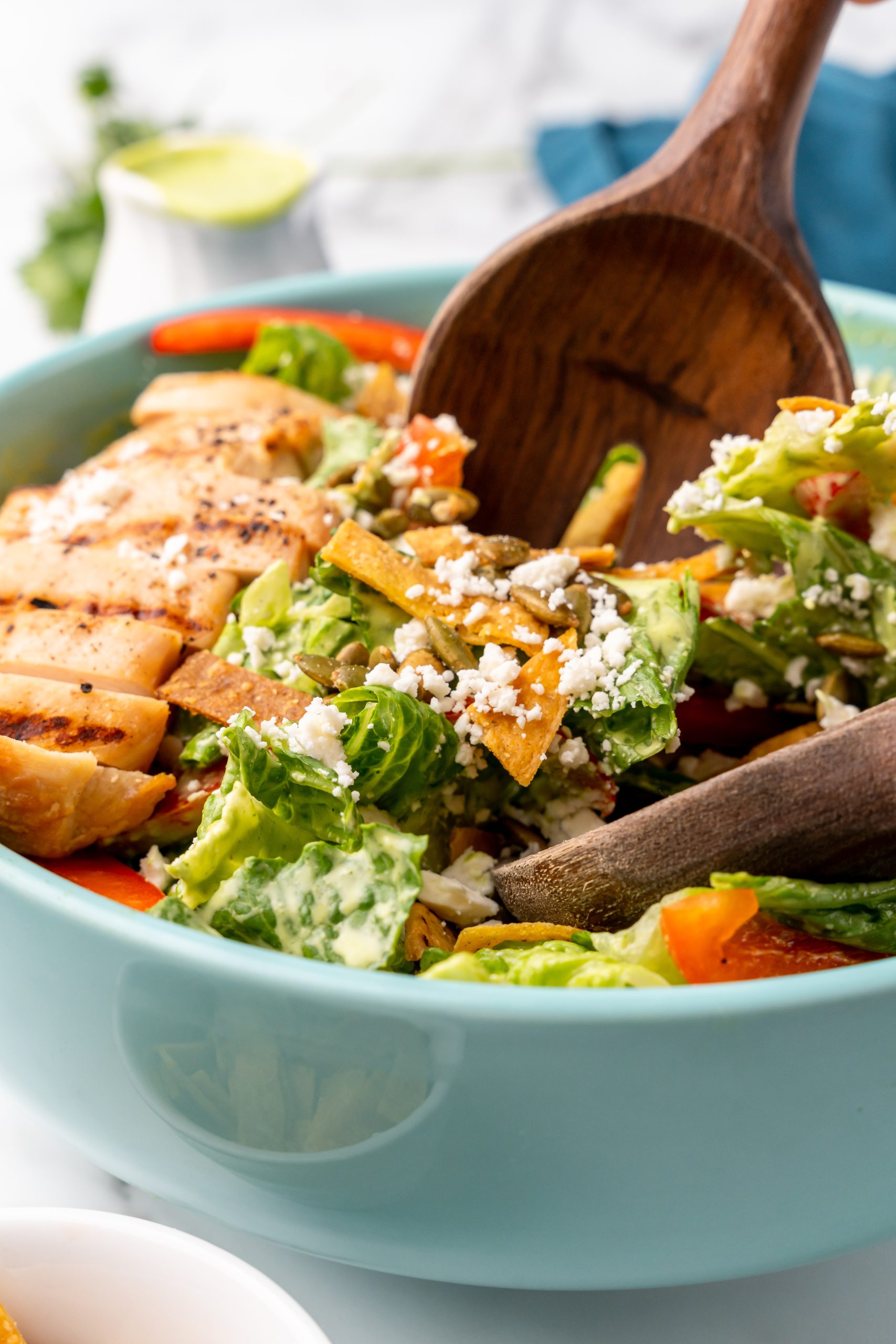 wooden utensils in a blue salad bowl filled with Mexican caesar salad