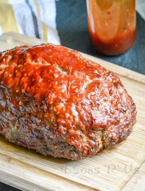 All Jack'd Up Stuffed Smoked Meatloaf shown on a wooden cutting board slathered in special sauce