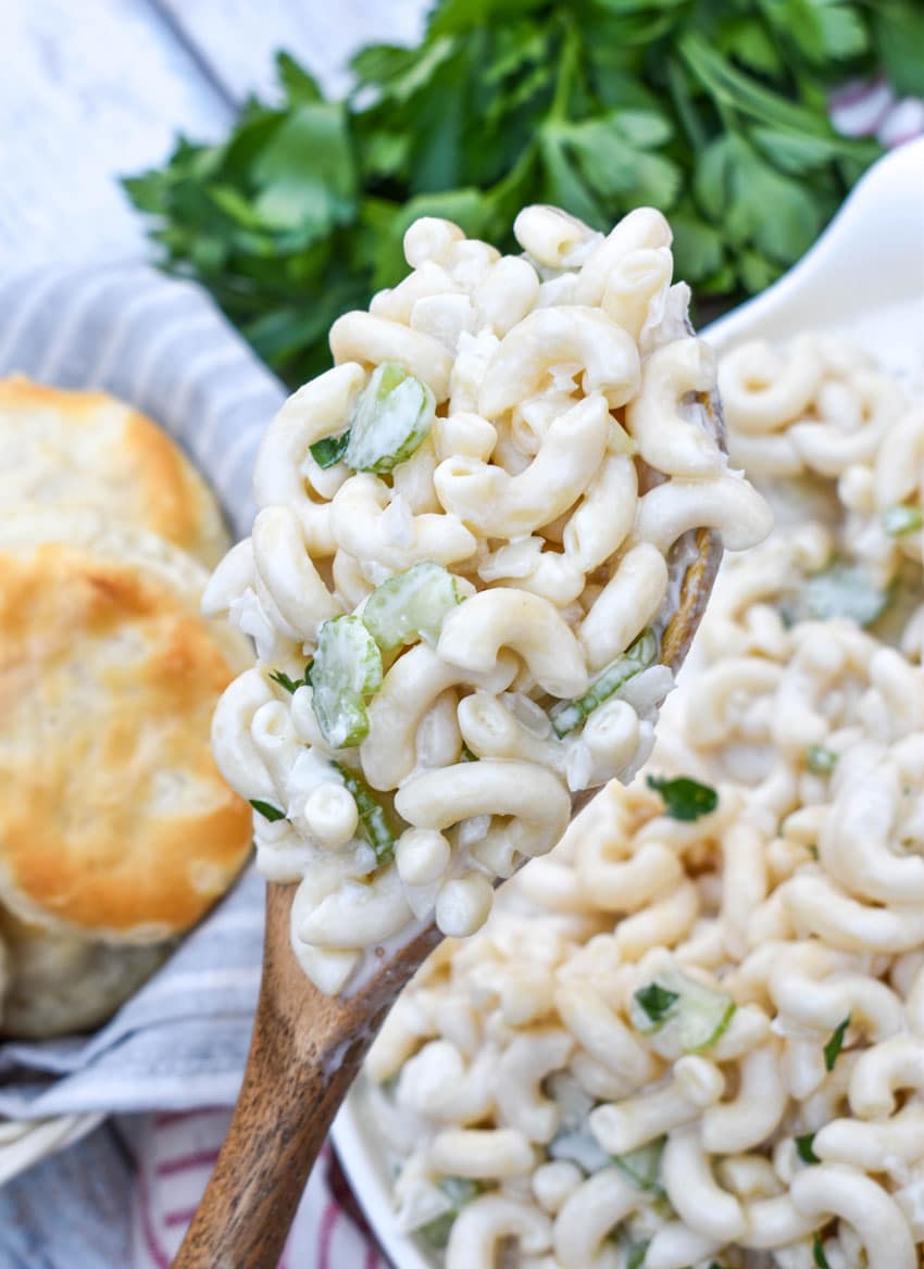 a wooden spoon holding up a scoop of homemade creamy macaroni salad