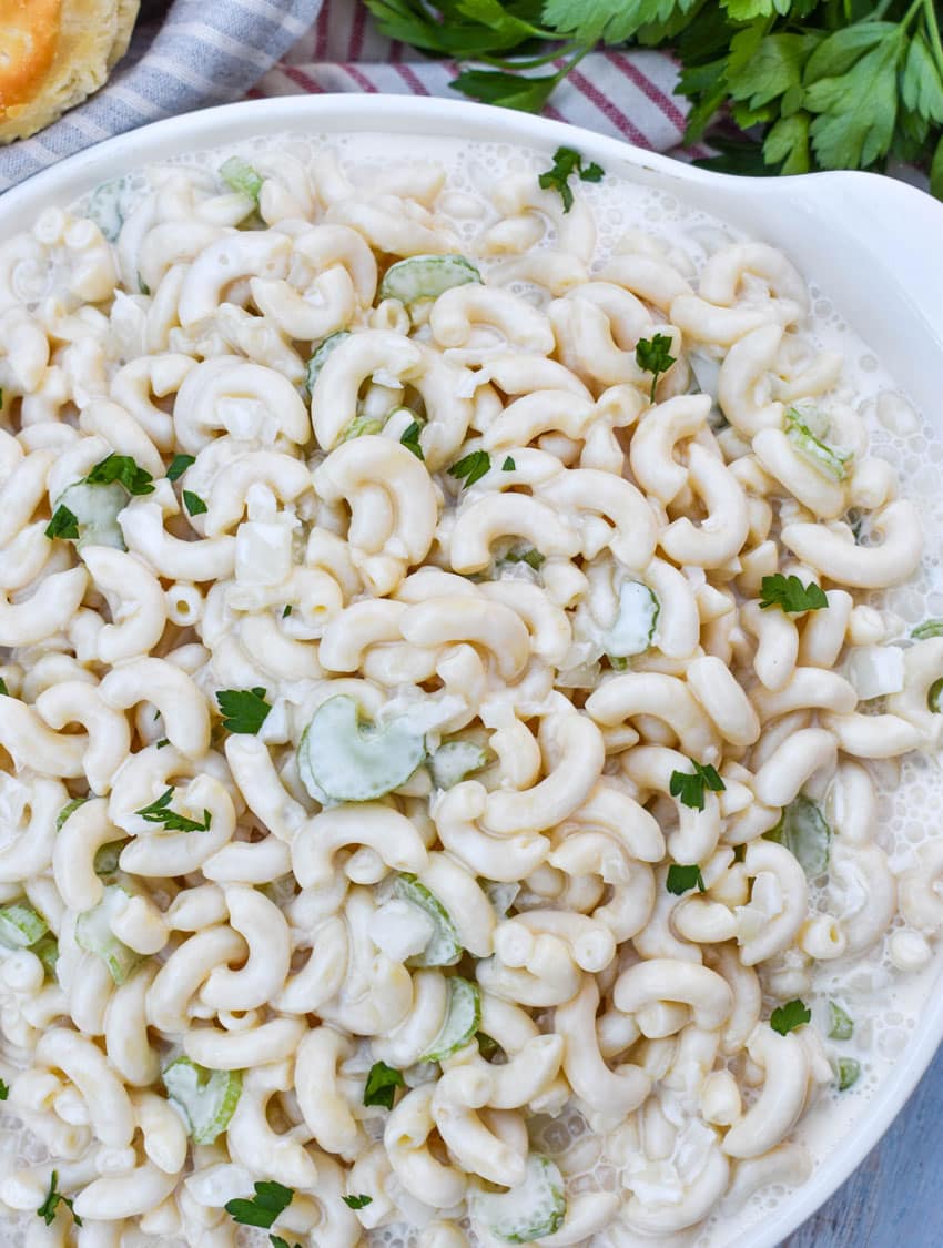aunt gert's sweet macaroni salad in a shallow white serving bowl with fresh herbs on the side
