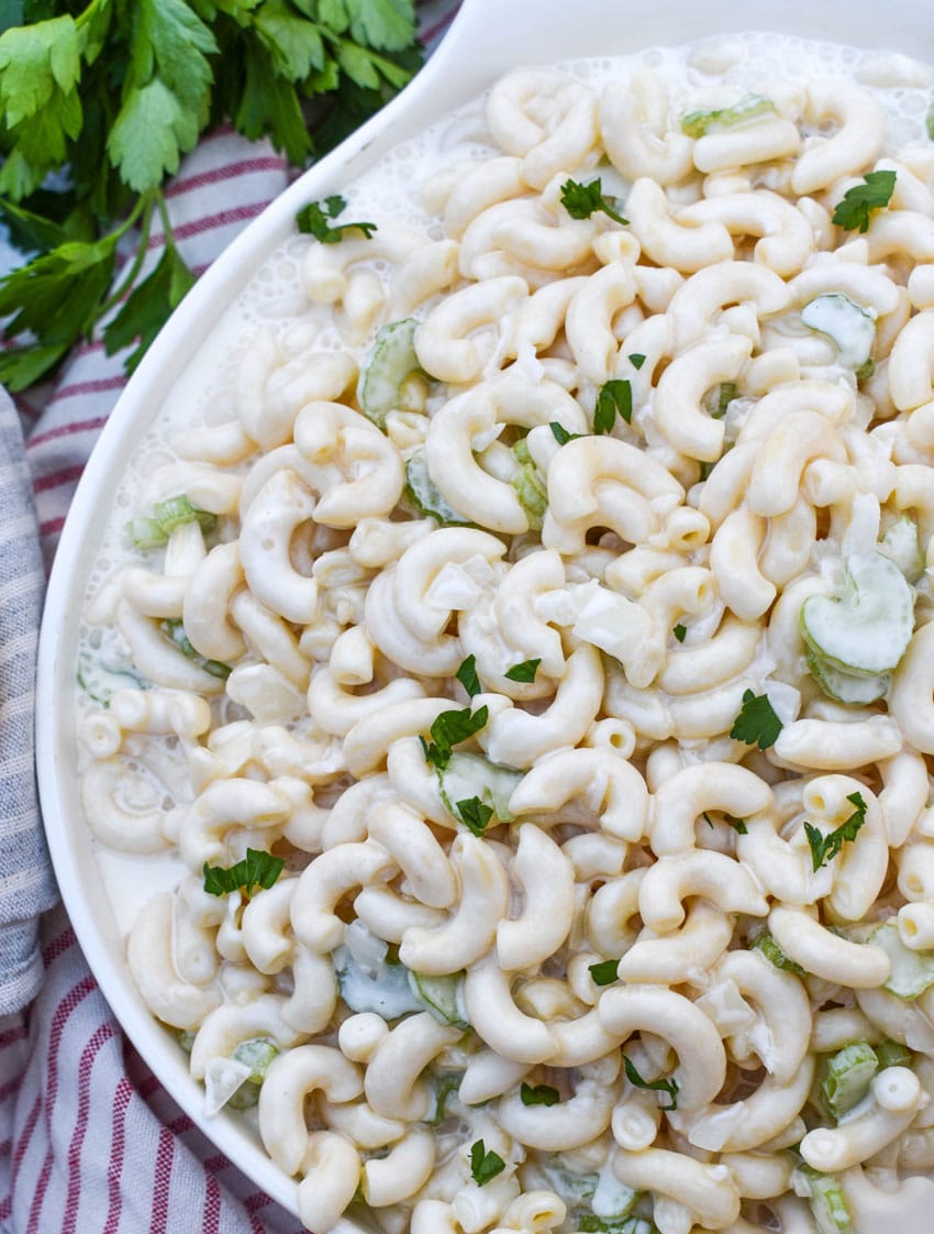 aunt gert's sweet macaroni salad in a shallow white serving bowl with fresh herbs on the side