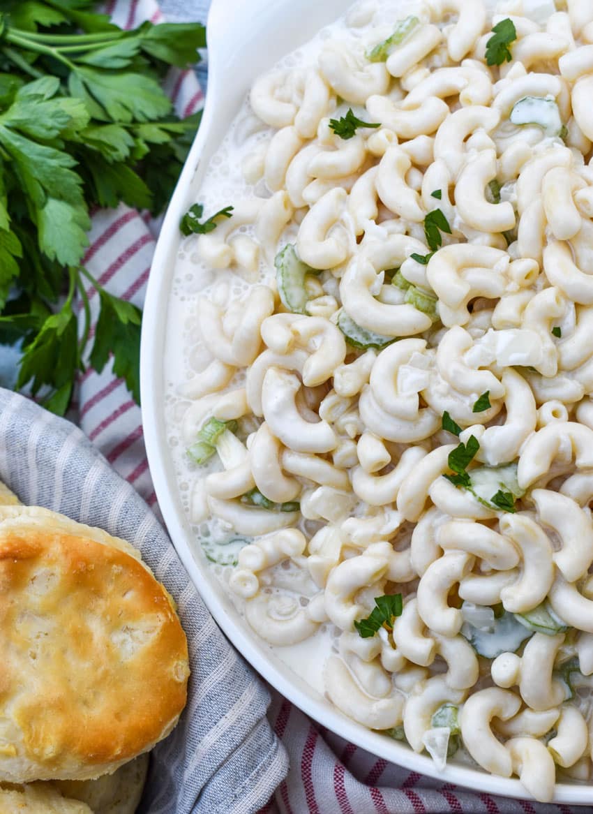 aunt gert's sweet macaroni salad in a shallow white serving bowl with fresh herbs on the side