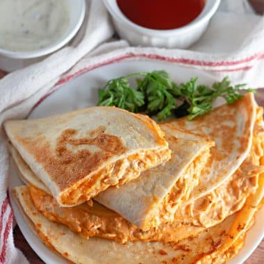 buffalo chicken quesadillas on a white plate with fresh herbs on the side