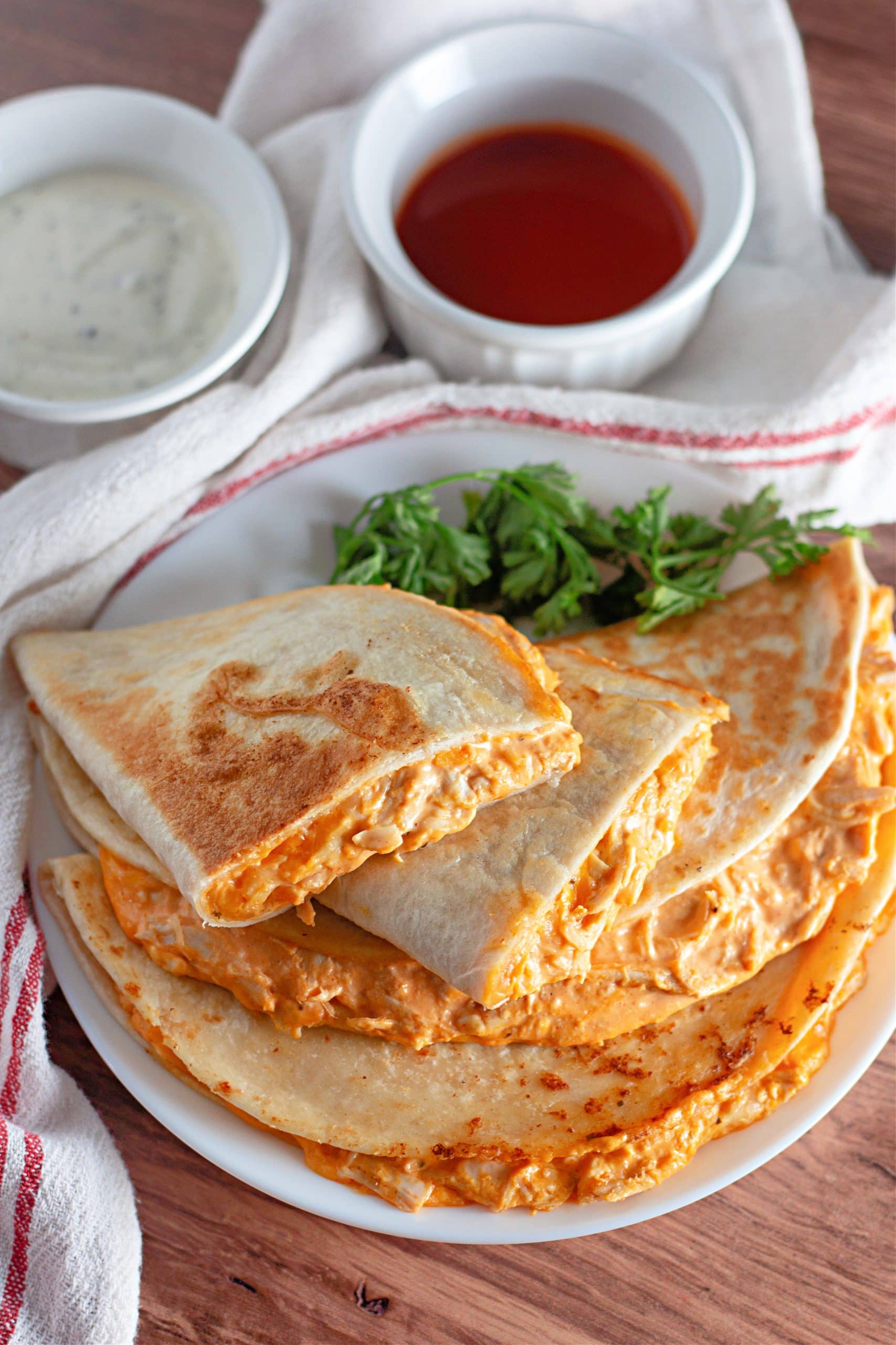 buffalo chicken quesadillas on a white plate with fresh herbs on the side