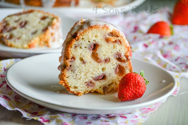 a slice of Glazed Strawberry Lemon Yogurt Cake shown on a white plate with a fresh strawberry