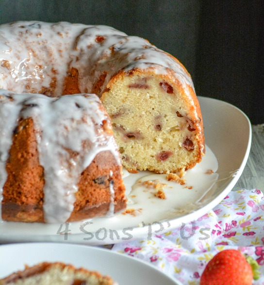 Glazed Strawberry Lemon Yogurt Cake shown on a white plate with a slice removed to show the inner cake crumb studded with pieces of strawberry