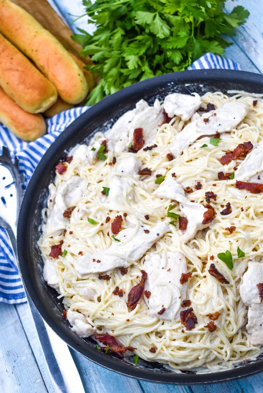 creamy chicken bacon caesar pasta in a black skillet with fresh herbs in the background