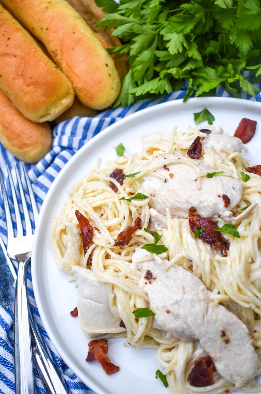 creamy chicken bacon pasta on a white plate with fresh herbs in the background
