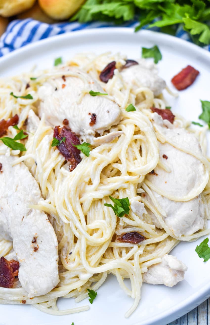creamy chicken bacon pasta on a white plate with fresh herbs in the background