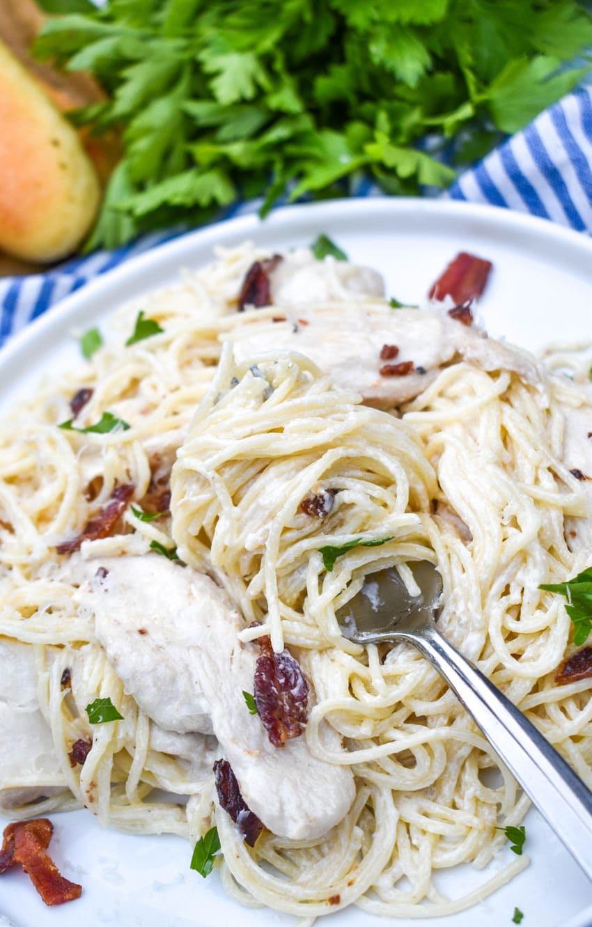 a silver fork wrapped in chicken bacon caesar pasta resting on a pile of pasta on a white plate