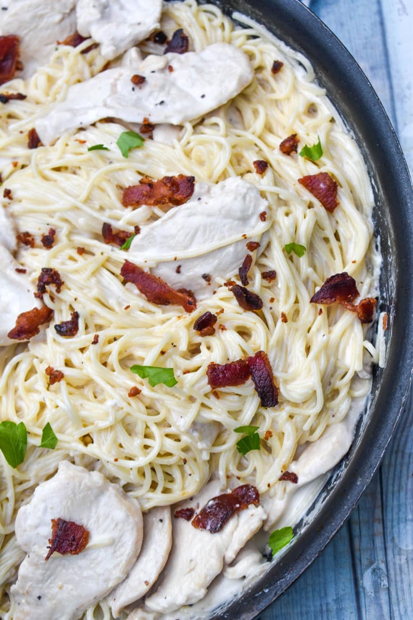 creamy chicken bacon caesar pasta in a black skillet with fresh herbs in the background