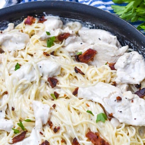 creamy chicken bacon caesar pasta in a black skillet with fresh herbs in the background