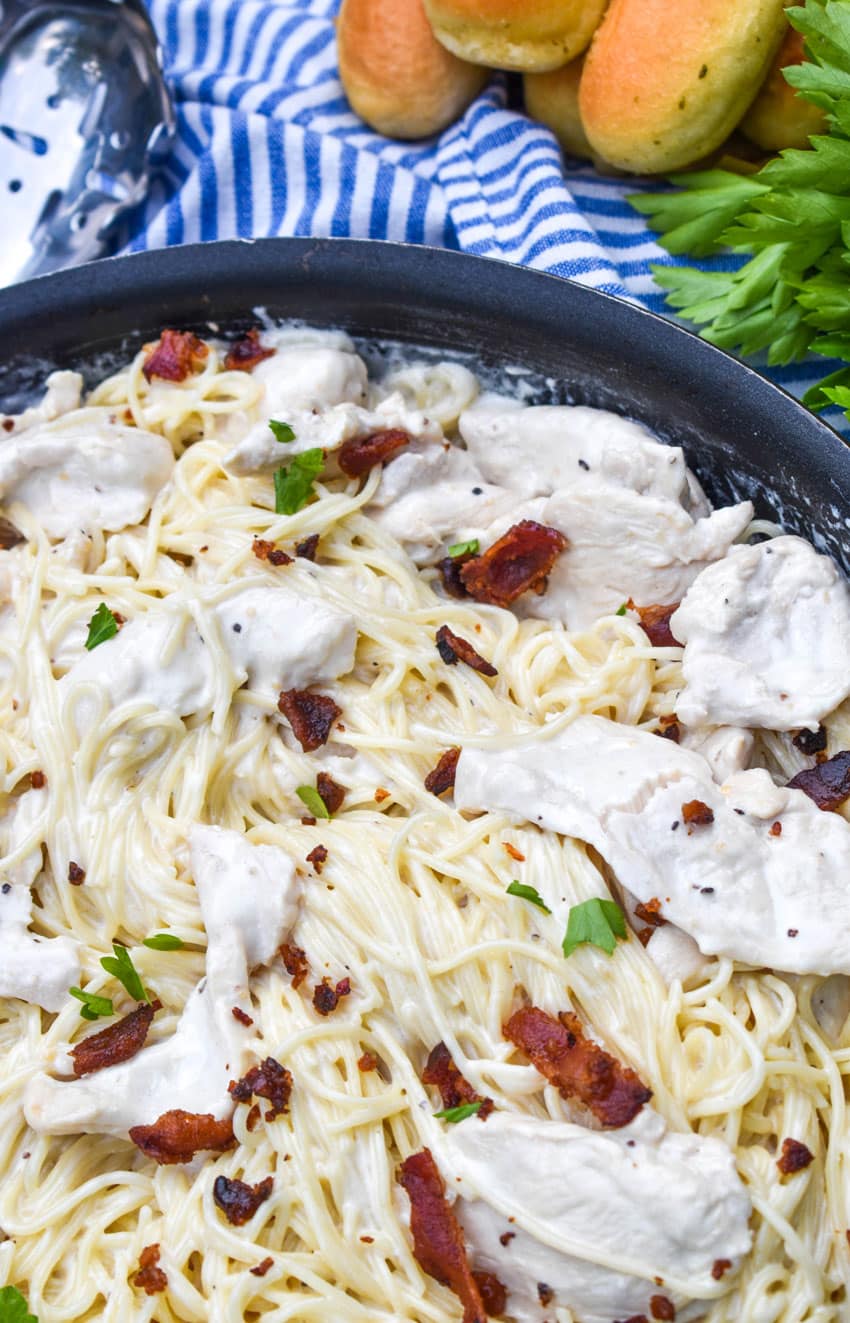 creamy chicken bacon caesar pasta in a black skillet with fresh herbs in the background