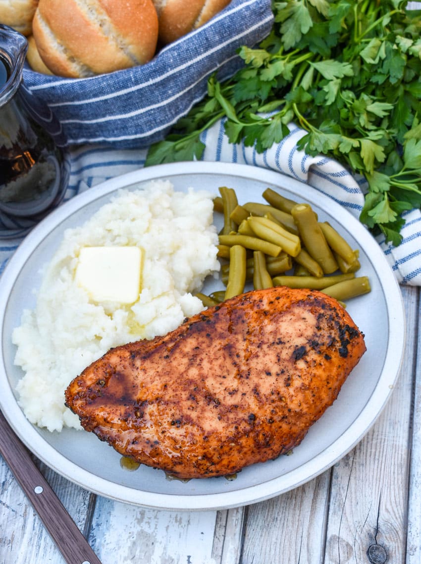 a maple chipotle smoked chicken breast next to mashed potatoes and canned green beans on a white plate