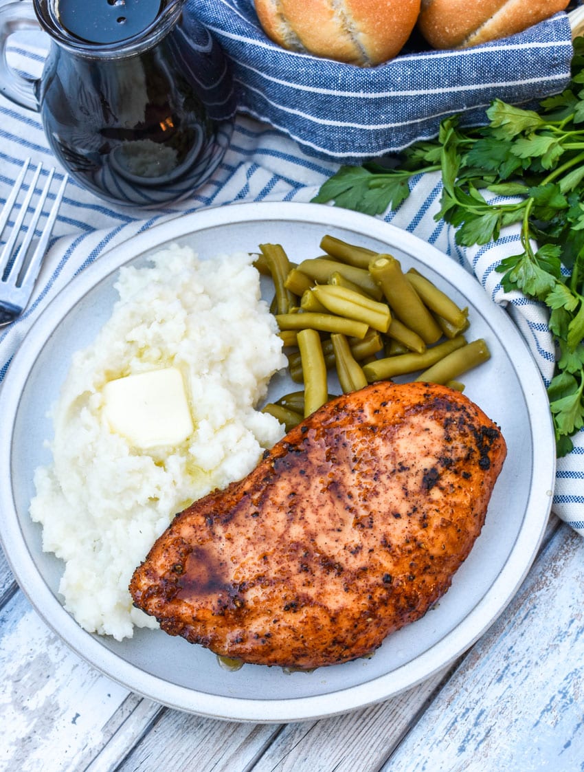 a maple chipotle smoked chicken breast next to mashed potatoes and canned green beans on a white plate