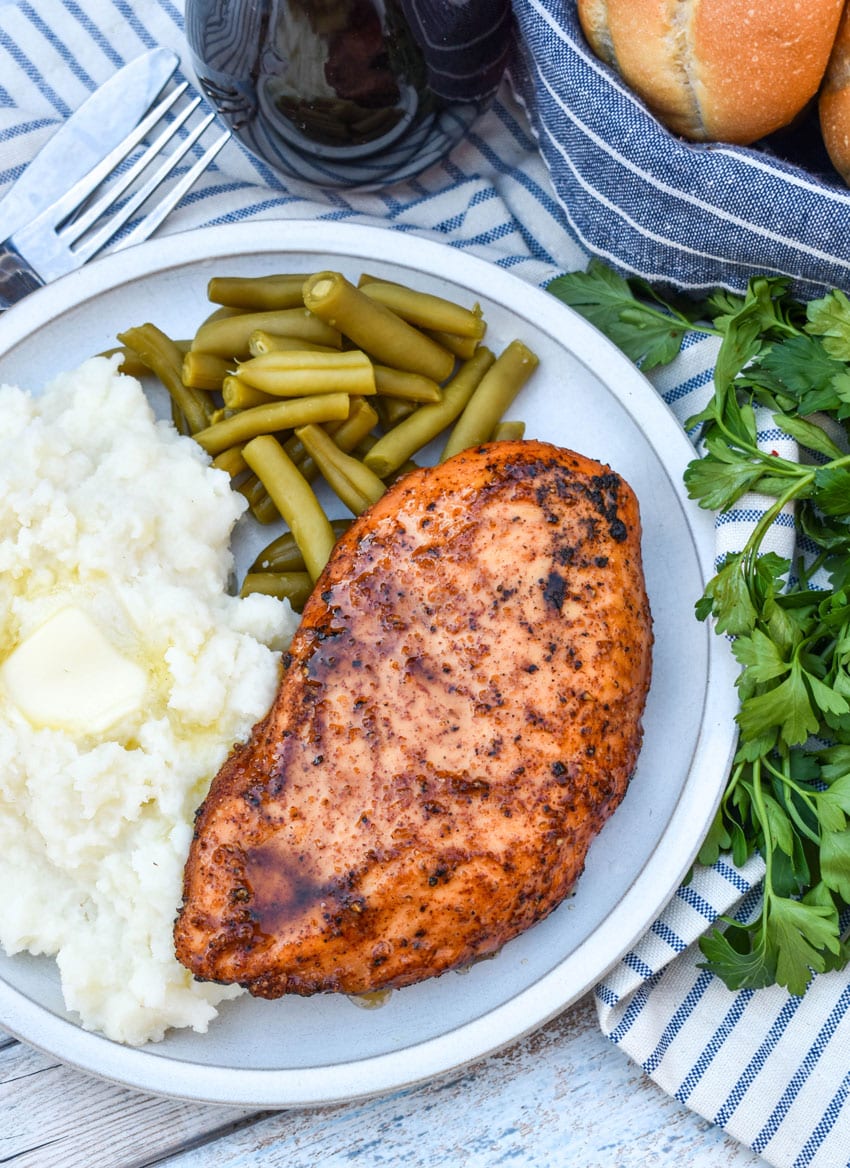 a maple chipotle smoked chicken breast next to mashed potatoes and canned green beans on a white plate