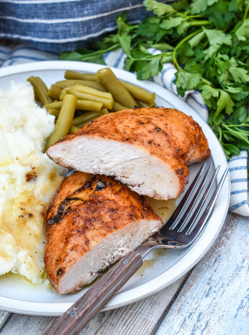 a maple chipotle smoked chicken breast next to mashed potatoes and canned green beans on a white plate