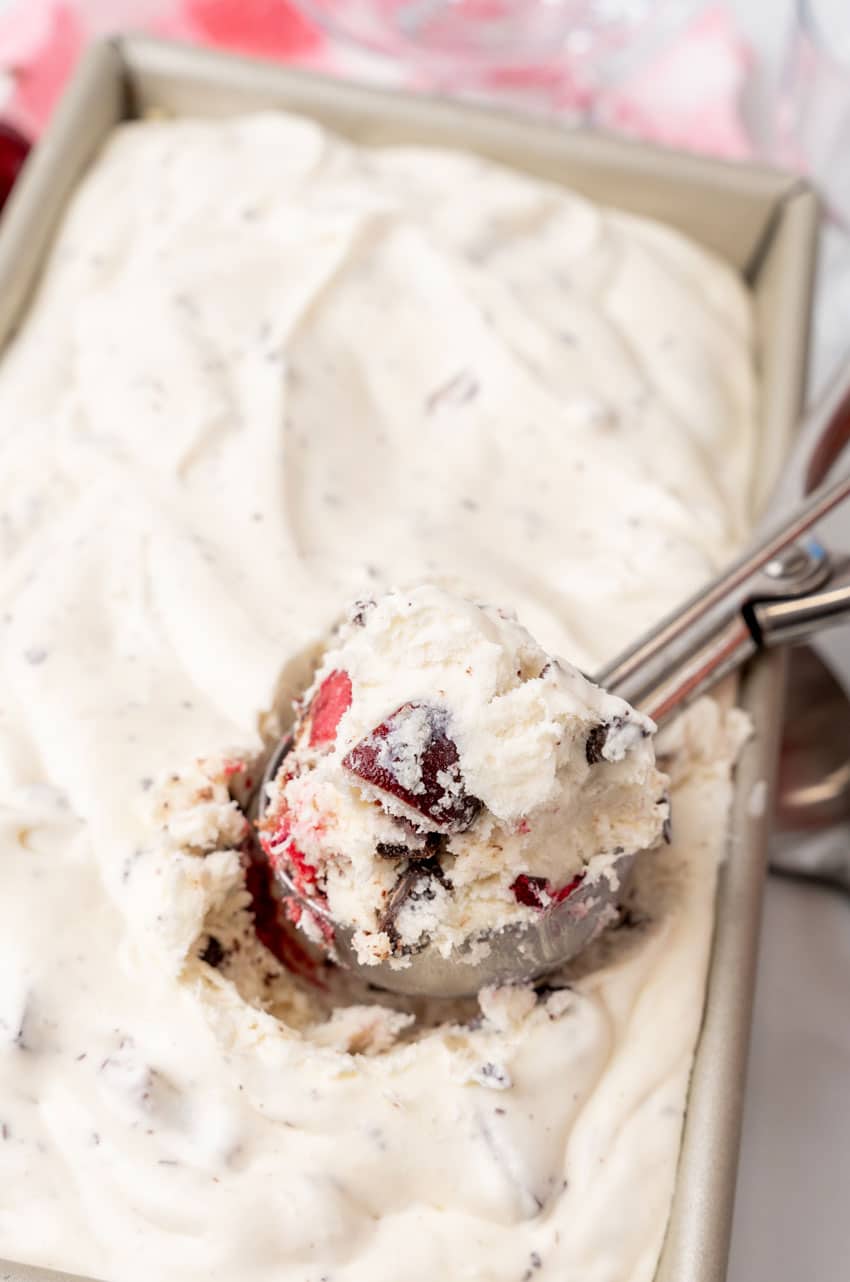 a silver cookie scooper scooping homemade chocolate cherry no churn ice cream out of a metal loaf pan