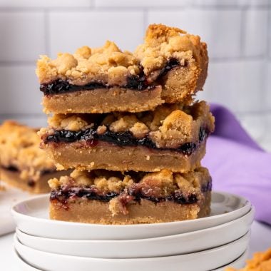 three peanut butter and jelly bars stacked on a small white plate