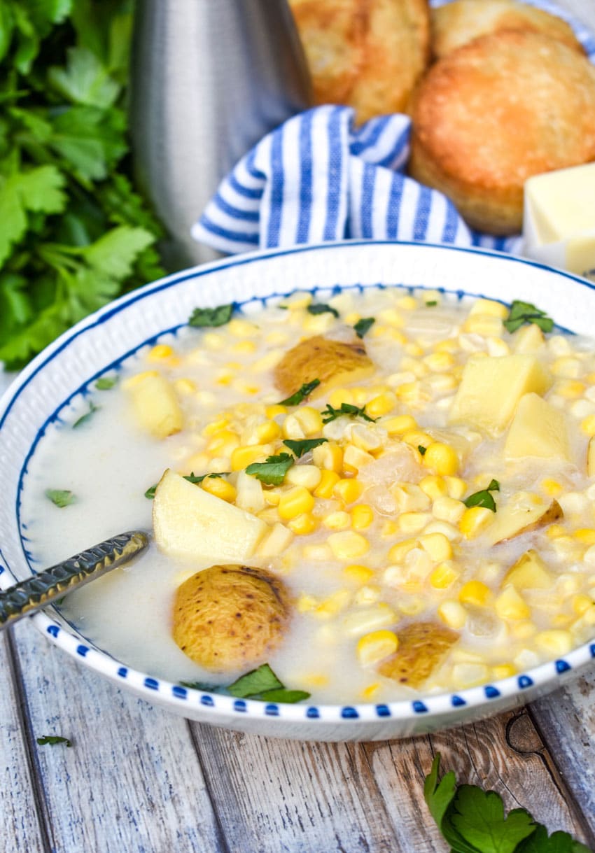 a silver spoon stuck in a white bowl filled with creamy corn soup