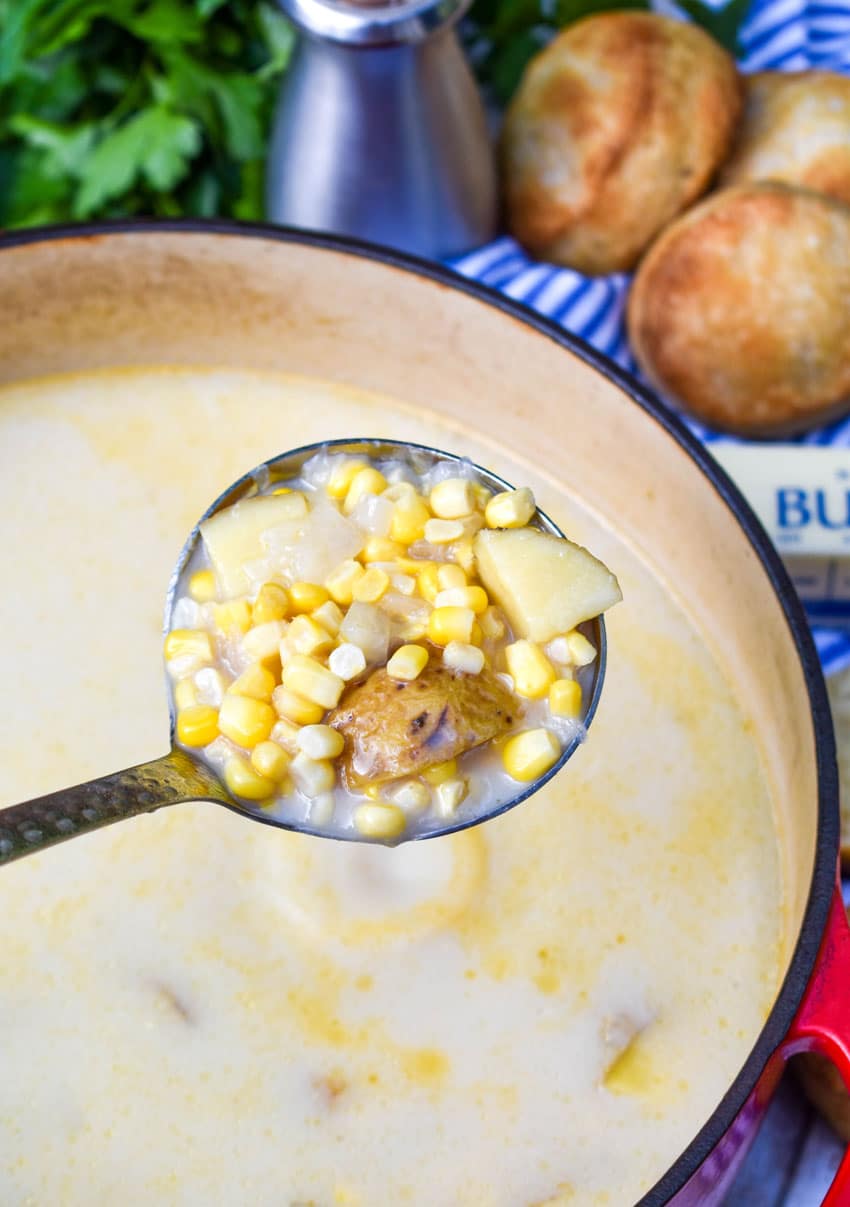 a silver ladle holding up a scoop of creamy corn & potato soup