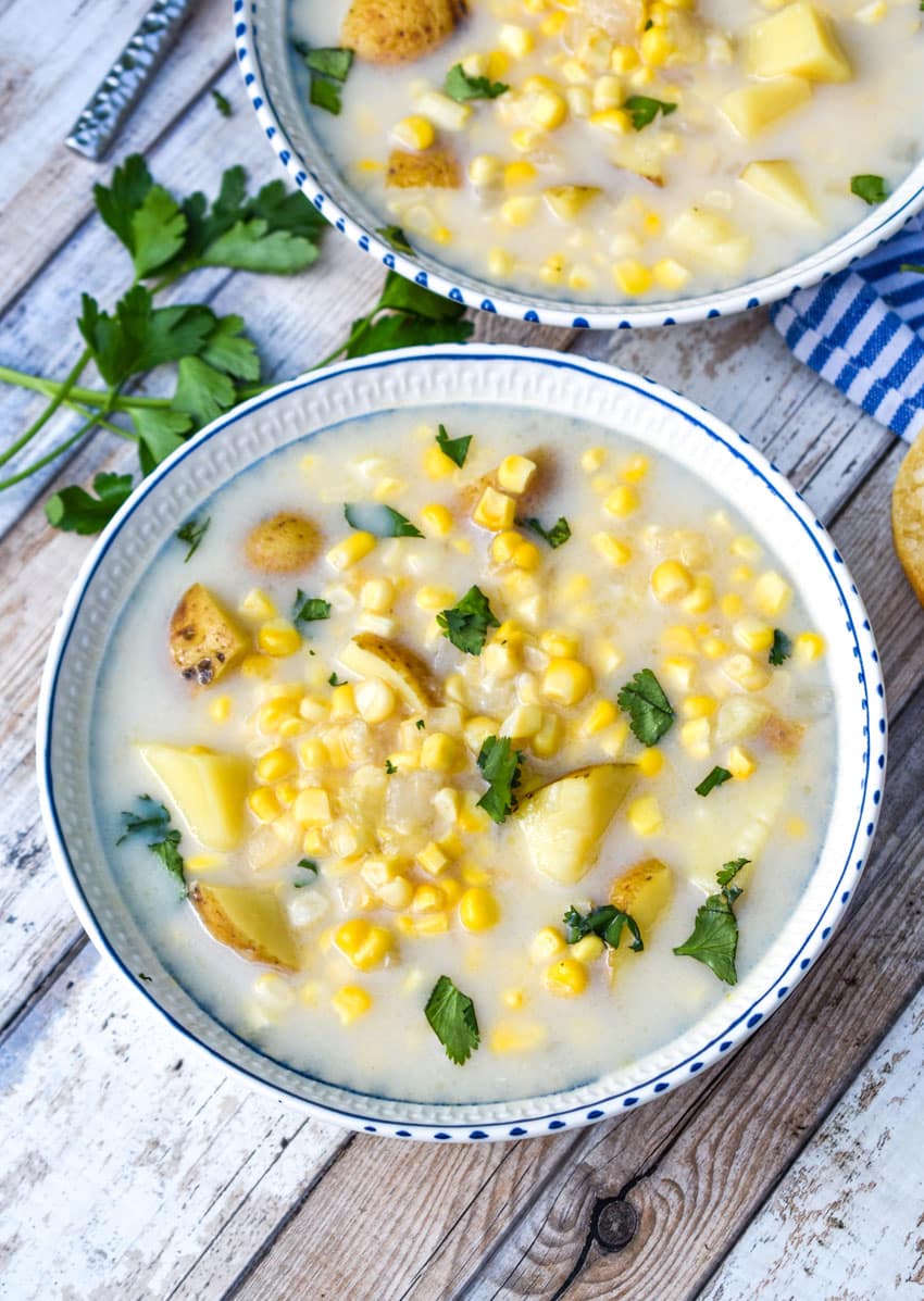creamy corn & potato soup in a white bowl garnished with fresh chopped green herbs