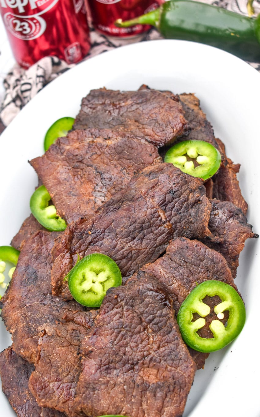 dr pepper jalapeno smoked beef jerky pieces with jalapeno slices in a white serving platter