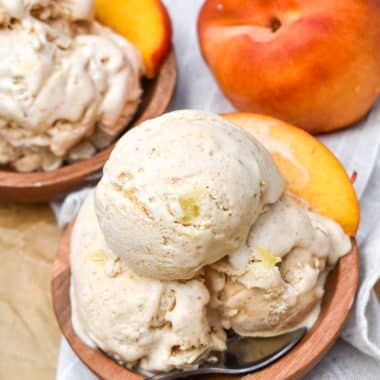 scoops of no churn peaches and cream ice cream in two small wooden bowls with fresh peaches in the background