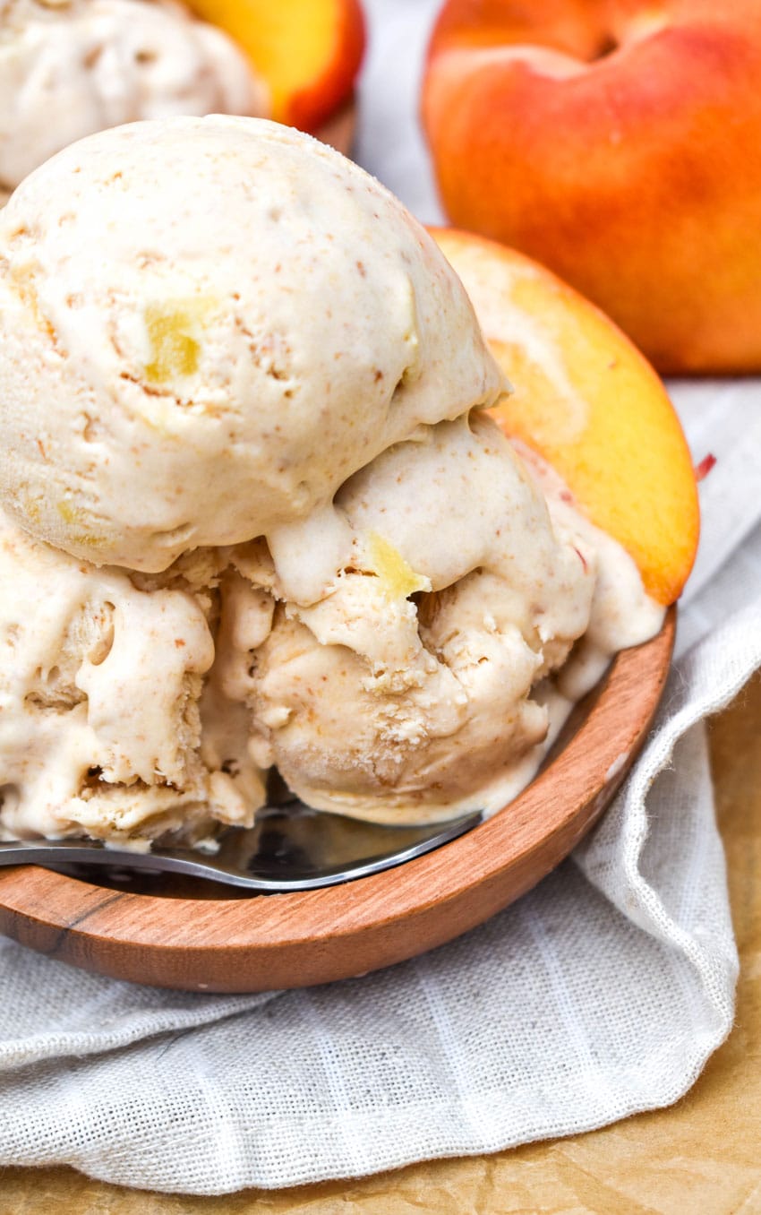 scoops of no churn peach ice cream in a small wooden bowl with a silver spoon on the side