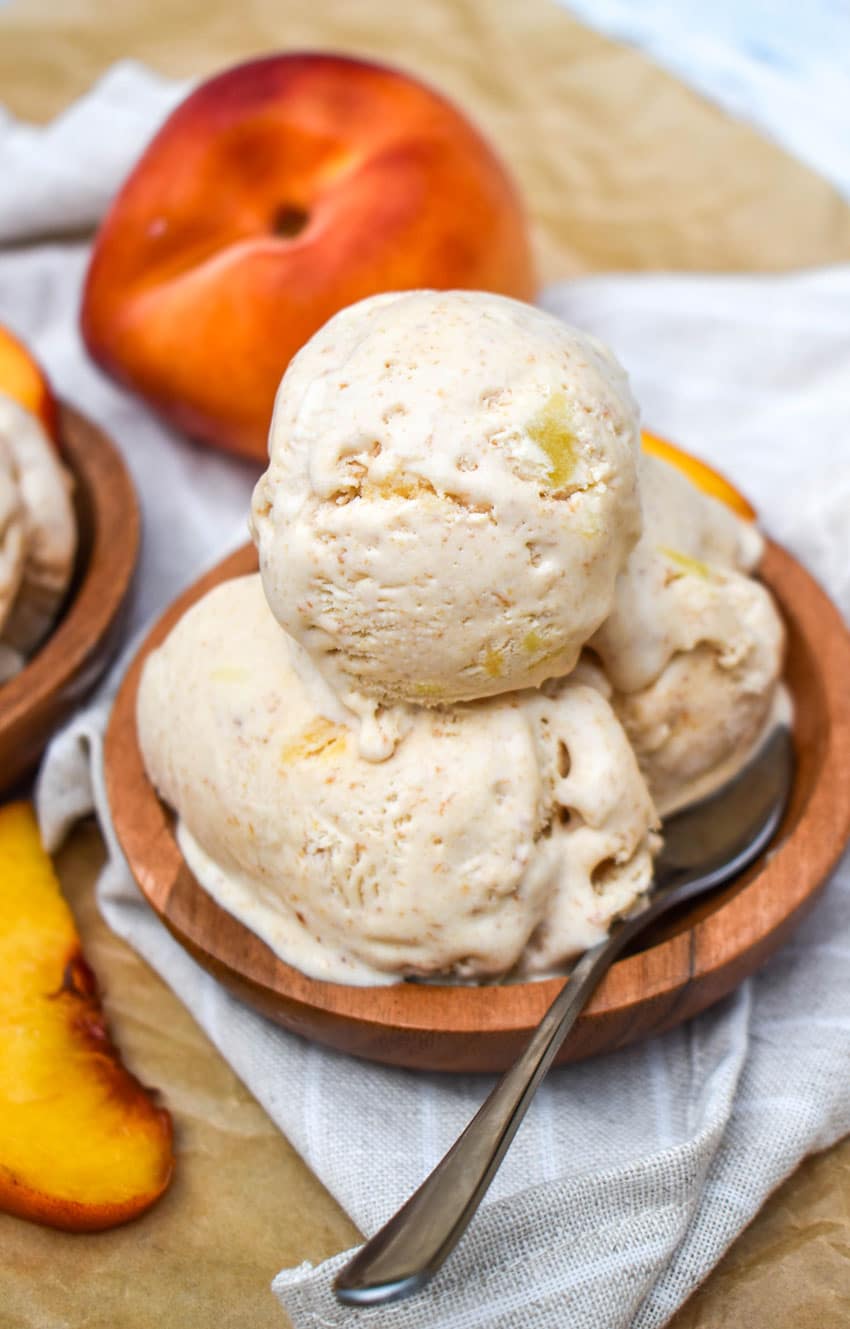 scoops of no churn peaches and cream ice cream in a small wooden bowl with a small silver spoon resting on the side